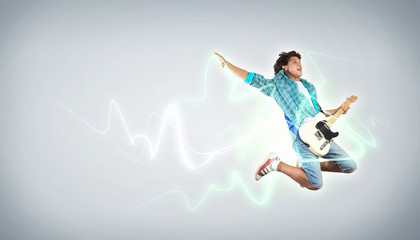 young man playing on electro guitar and jumping