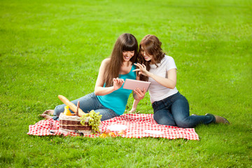 Two women in the park on a picnic with a Tablet PC