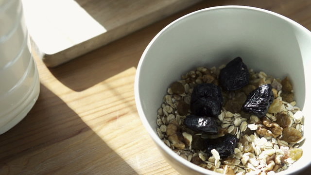 Hand adding prune and cranberries to muesli in bowl