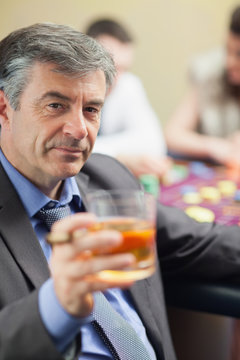 Man lifting glass of whiskey at roulette table