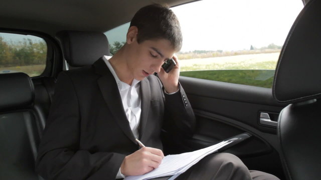 Businessman viewing documents and talikng on the phone in car