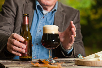Senior man enjoying dark beer and cheese in autumn forest.