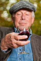 Senior man enjoying red wine in autumn forest.