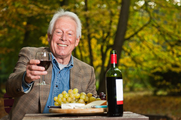 Senior man enjoying red wine in autumn forest.