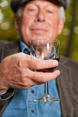 Senior man enjoying red wine outdoors in autumn forest.