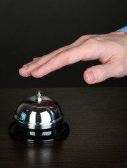 Hand ringing in service bell on wooden table on black