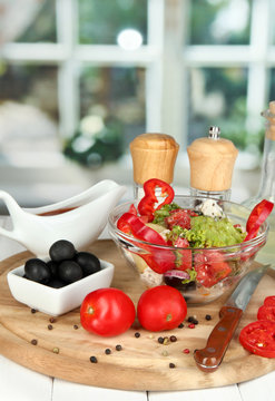 Fresh greek salad in glass bowl surrounded by ingredients for