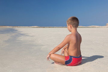 The little boy meditating on the beach
