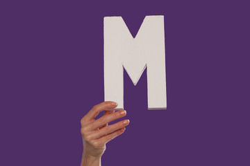 Female hand holding up the letter M from the bottom