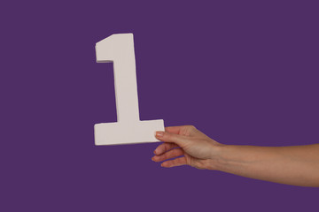 Female hand holding up the number 1 from the right