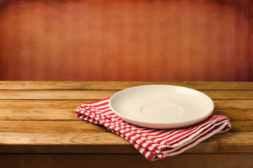 Empty white plate on wooden table over red grunge background