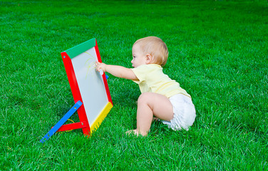 А beautiful little boy draws sitting on a lawn
