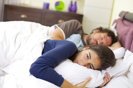 Young woman crying in bed desperate about man sleeping