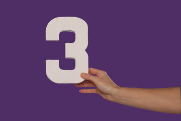 Female hand holding up the number 3 from the right
