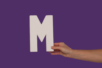 Female hand holding up the letter M from the right