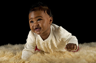Pretty baby girl crawling on fur rug.