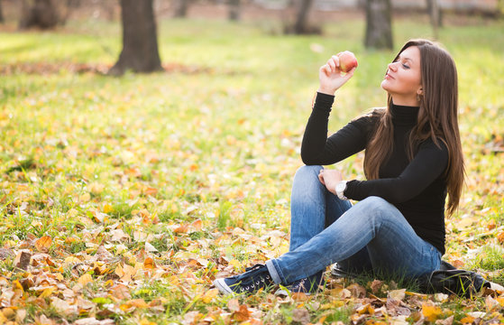 Portrait of beautiful young woman with apple in autumn park