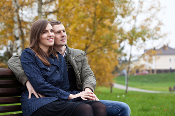 young couple sitting on bench in autumn park