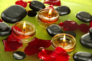 spa stones with rose petals and candles in water on plate