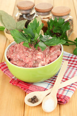 Bowl of raw ground meat with spices on wooden table