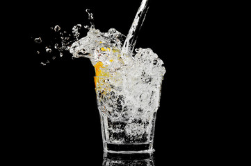 splash in a glass with lemon and ice on a black background