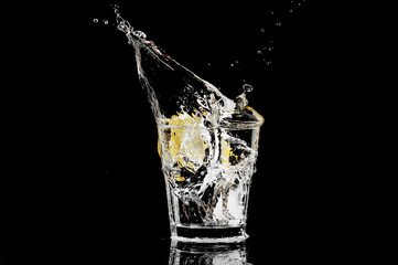 splash in a glass with lemon and ice on a black background