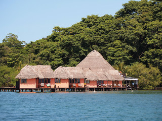 Tropical resort with thatched bungalows over the water and lush trees in background, Central America, Panama