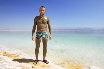 Male in mineral mud is on the shores of the dead sea in Israel