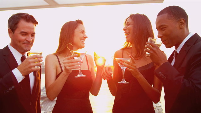 Two women drinking cocktails with men at luxury sunset party dressed in black 