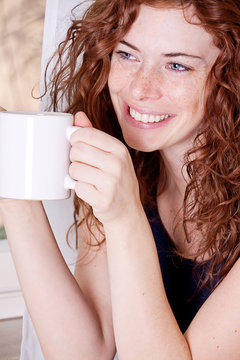 Junge h&uuml;bsche Frau mit Sommersprossen trinkt eine Tasse Kaffee