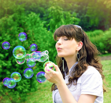 romantic young girl inflating colorful soap bubbles