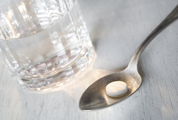 Pill on a spoon with a glass of water