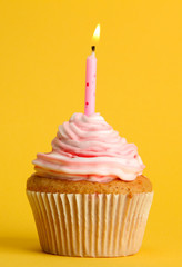 tasty birthday cupcake with candle, on yellow background