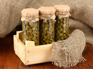 Glass jars with tinned capers on sack background close-up