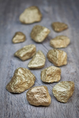 Gold nuggets scattered stones on wooden texture.