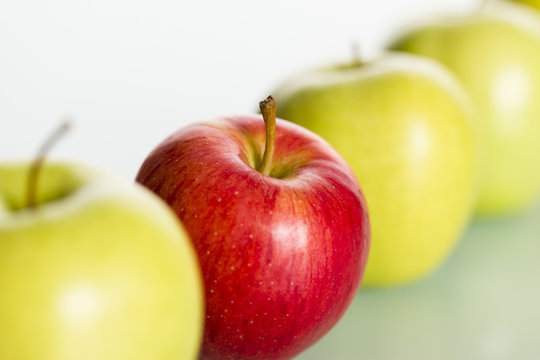 Red Apple Standing Out From Row Of Green Apples.