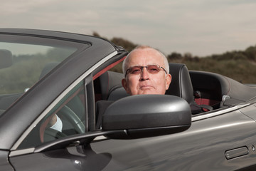 Fototapeta na wymiar Starszy przystojny szczęśliwy emerytowany mężczyzna prowadził swój samochód sportowy