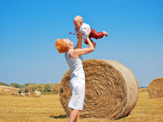 Young woman and little son on the field with big hay bale rolls