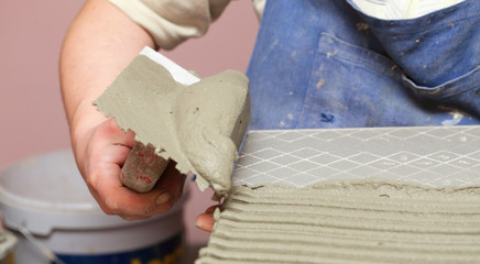 Construction worker is tiling at home tile floor adhesive