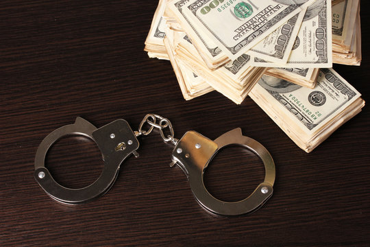 Handcuffs and packs of dollars on wooden table close-up