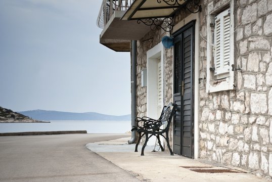 Fototapeta Old street of stone houses with bench by the sea