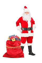 Santa Claus posing next to a bag full of gifts