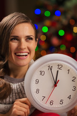 Portrait of happy woman showing clock in front of Christmas ligh
