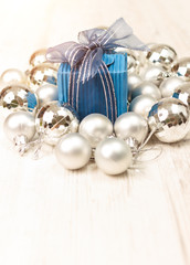 Perspective view of blue giftbox surrounded by silver baubles