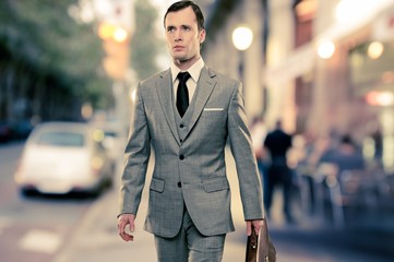 Man in classic grey suit with briefcase walking outdoors