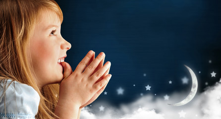 Portrait of little smiling praying girl in blue dress against da © Milles Studio