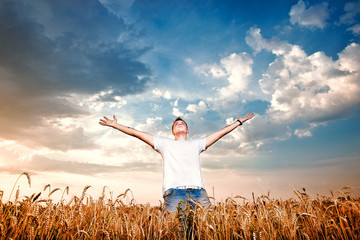 Happy man standing with open arms on a wheat field