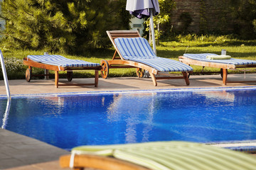 deck chairs on the edge of the beautiful blue pool filled with w