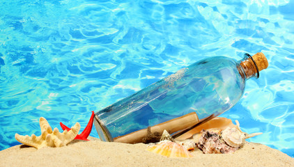 Glass bottle with note inside on sand, on blue sea background