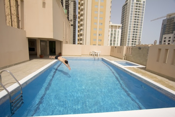 Obraz na płótnie Canvas Mężczyzna pływania w basenie na dachu mieszkania, Bahrajn